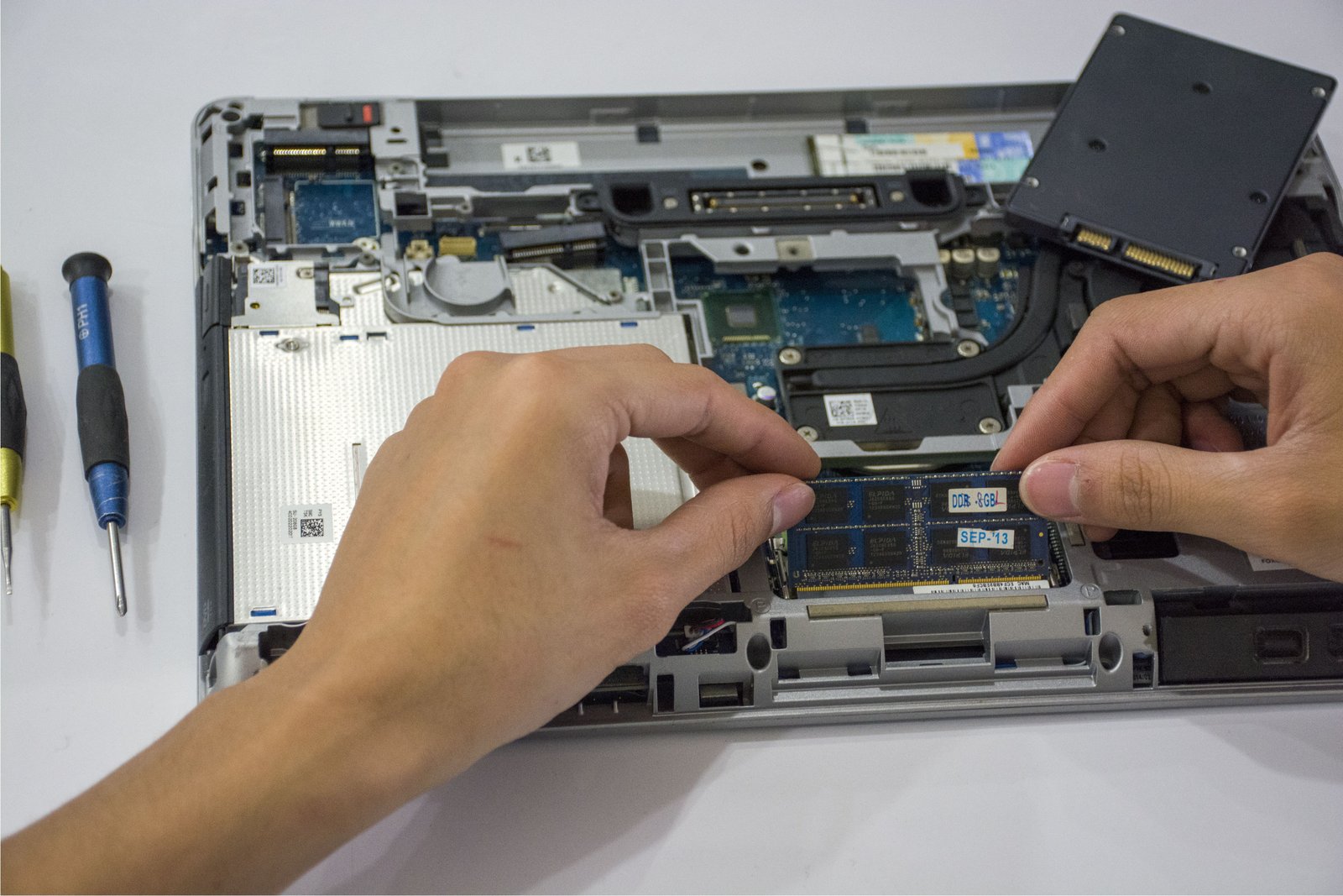 Hands repairing the internal parts of an open laptop on a desk, tools in frame