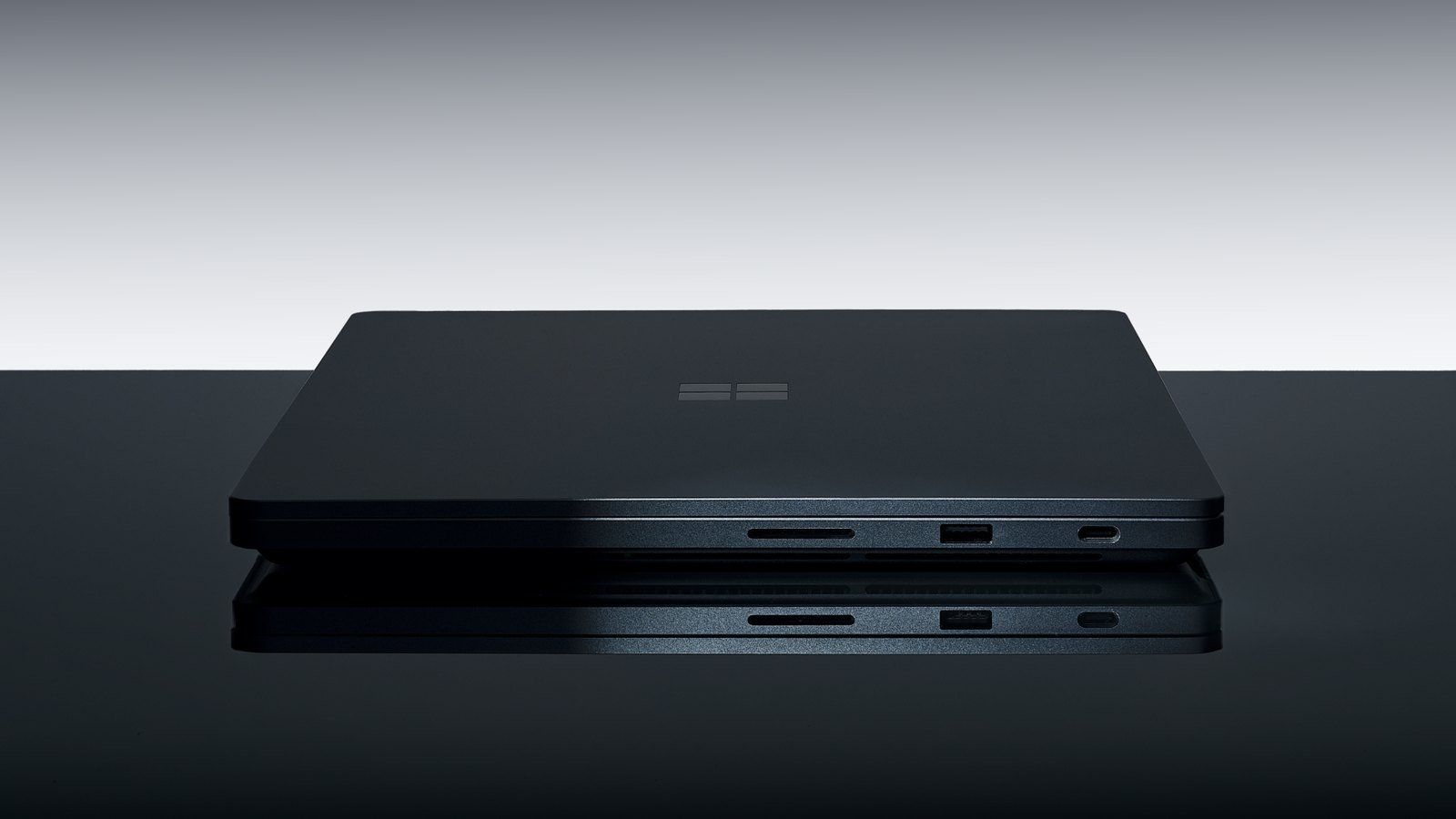 A closed dark Surface Laptop Ultra shown edge-on with an SD card slot, USB-A port, and USB-C port visible along one side, reflected on a glossy black surface
